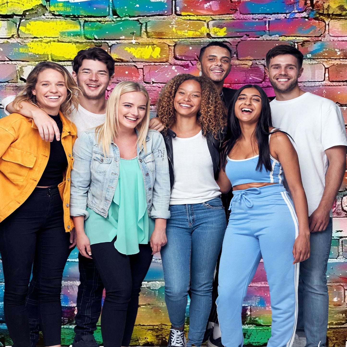 A group of six people stands close together and smiles in front of a colorful, graffiti-covered brick wall backdrop 7x5ft Fabric Graffiti Brick Wall Backdrop for Photography Hip Hop Disco Background Party Banner Portraits Photoshoot Props by ideasbackdrop.