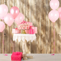 A small white table with a lace cloth holds pink flowers and gift boxes, surrounded by pink balloons, set against an ideasbackdrop Brown Wood Backdrops for Photography Vintage Brown Background Baby Shower Birthday Photo Booth Studio Props made vivid through high-resolution printing technology.