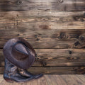 A brown cowboy hat and pair of boots are placed in front of a 7x5ft Vintage Wood Backdrop Retro Rustic Wooden Floor Background for Photography Photo Booth Video Shoot Studio Props by ideasbackdrop, creating a classic Western look with wide applications for various themed events.