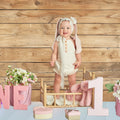 A smiling baby stands in a wooden crate, surrounded by pink flowers, a pink stuffed bunny, and decorative blocks spelling "ONE." The scene celebrates a first birthday against an ideasbackdrop 7x5ft Wooden Backdrop Baby Shower Wood Wall Background Party Decorations Props for Photographers Studio with high-resolution printing for stunning clarity.