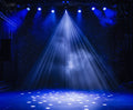 A stage illuminated by multiple blue spotlights with a misty atmosphere, enhanced by a stunning ideasbackdrop 7x5FT Stage Spotlight Backdrop Concert Gloomy Night Scenic Photography Background Portrait Studio Props printed in high-resolution on the stage wall backdrop.