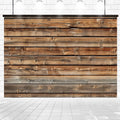 A **7x5ft Wood Backdrops for Photography Worn Wooden Boards Background Brown Photo Wall Photo Studio** by **ideasbackdrop** with horizontal planks in various shades of brown against a tiled floor and white brick background, perfect for high-resolution printing as wood backdrops with wrinkle resistance. The scene is illuminated by ceiling lights.