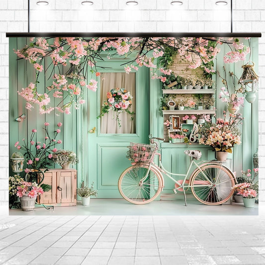 A pastel green door surrounded by ultra-realistic pink flowers and plants, with a white bicycle adorned with blooms positioned in front. Shelves on the right hold more plants and decorative items, creating a Bicycle Blossom Photography Flower Backdrop-ideasbackdrop that’s perfect for capturing memorable moments.