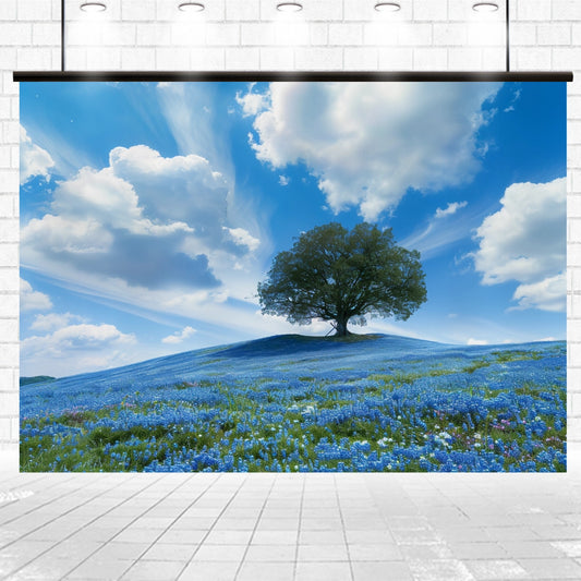 A large photograph of a lone tree on a hill covered with blue flowers under a sky with scattered clouds creates a stunning focal point on the white brick wall. This Blue Sky Flowers Cover Old Tree Floral Backdrop by ideasbackdrop makes for an exceptional professional photography background.