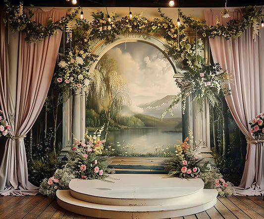 A decorated wedding arch featuring a Bridal Shower Photography Floral Background - ideasbackdrop and curtains, set against a scenic backdrop of a lake with mountains, trees, and a cloudy sky. A small wooden stage is positioned beneath the arch.