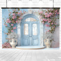 Pale blue double doors with intricate designs are framed by pink climbing roses and white vases on either side, set against a backdrop of the Floral Blue Door Wall Bridal Shower Backdrop -ideasbackdrop that emphasizes botanical magnificence.