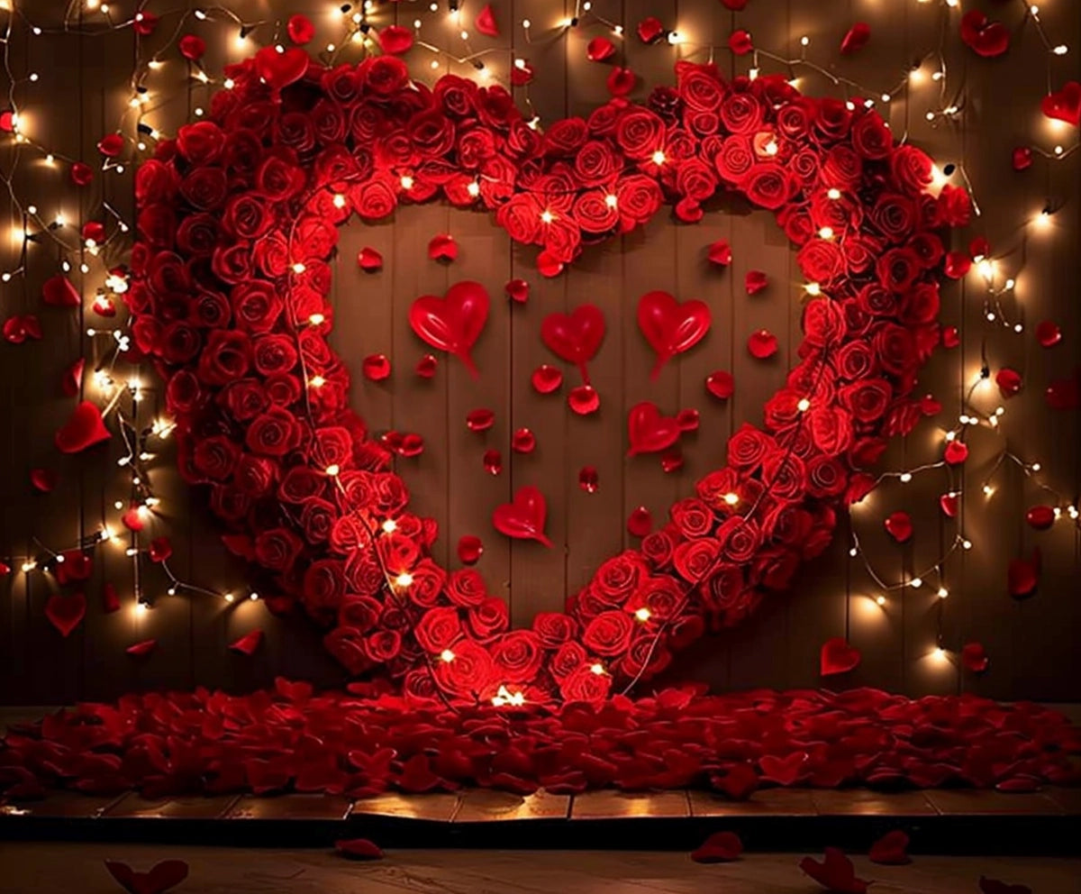 A large heart shape made of red roses is mounted on a wall, surrounded by string lights. Red rose petals and smaller heart decorations are scattered around, creating a Floral Wall Valentine's Day Flower Background - ideasbackdrop.