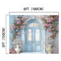 A blue ornate double door surrounded by pink flowers and white vases with greenery, presenting a scene of Floral Blue Door Wall Bridal Shower Backdrop -ideasbackdrop, measuring 6 feet in width and 5 feet in height.