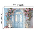 An ornate blue double door surrounded by decorative columns and pink floral arrangements exudes botanical magnificence. The **Floral Blue Door Wall Bridal Shower Backdrop -ideasbackdrop** by **ideasbackdrop**, with dimensions 7ft (210cm) by 5ft (150cm), is noted above and to the left side of the door.