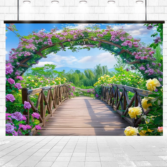 A **Flowers Blossom Wooden Bridge Floral Backdrop-ideasbackdrop** adorned with vibrant pink, purple, and yellow flowers, framed by a floral arch, leads to a scenic view of trees and mountains under a partly cloudy sky—ideal for weddings or any events seeking a vivid floral backdrop by **ideasbackdrop**.