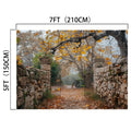 An open gate with stone walls leads to a path covered in autumn leaves, with a bicycle leaning against a tree in the background. Perfect for fall portraits, the gate's dimensions are marked as 7ft (210cm) wide and 5ft (150cm) tall, creating an ideal Gate Stone Wall Autumn Leaves Trees Fall Backdrop-ideasbackdrop by ideasbackdrop.