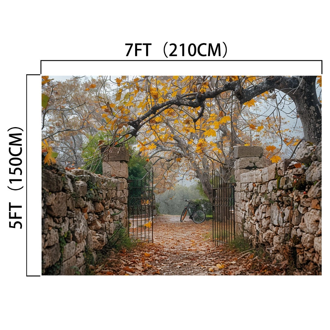 An open gate with stone walls leads to a path covered in autumn leaves, with a bicycle leaning against a tree in the background. Perfect for fall portraits, the gate's dimensions are marked as 7ft (210cm) wide and 5ft (150cm) tall, creating an ideal Gate Stone Wall Autumn Leaves Trees Fall Backdrop-ideasbackdrop by ideasbackdrop.
