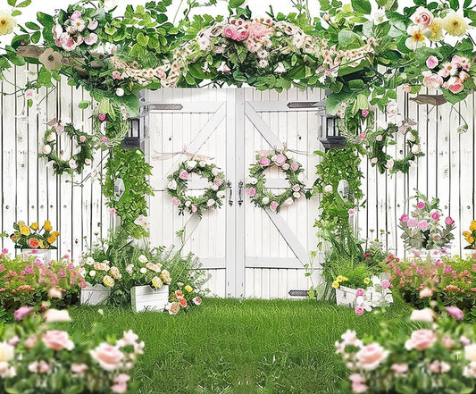 A white wooden fence with double gates is decorated with pink and white flowers and greenery, creating a beautiful Green Leaves Butterfly Spring Floral Backdrop from ideasbackdrop. Various potted plants and flowers are arranged on the grass in front of it, adding to the natural elegance of the scene.