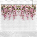 A high-resolution Pink Bridal Brick Romantic Floral Backdrop - ideasbackdrop featuring a white brick wall adorned with cascading pink flowers, set in a tiled floor space—perfect for engagement photos.