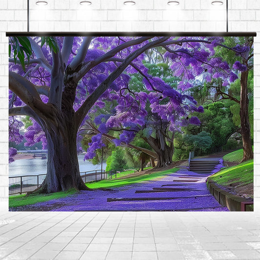 A park scene with large trees covered in vibrant purple blossoms, a pathway surrounded by green grass, and a calm body of water in the background creates an ideasbackdrop Purple Tree Branches Leaves Scenic Backdrop-ideasbackdrop rich with lifelike landscapes.