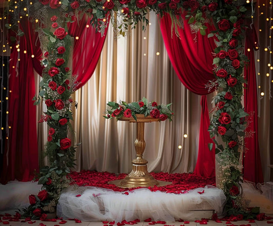 A gold pedestal is surrounded by red roses, red drapes, and fairy lights, set on a stage with red petals on the floor and complemented by a Red Floral Wedding Bridal Shower Backdrop -ideasbackdrop.