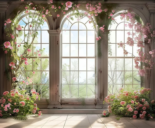 A sunlit room with large arched windows adorned with climbing pink flowers exudes floral elegance. The windows overlook a serene, green landscape, creating a perfect wedding backdrop. For such an occasion, the Romantic Bridal Shower Window Flower Backdrop by ideasbackdrop makes an exquisite choice.