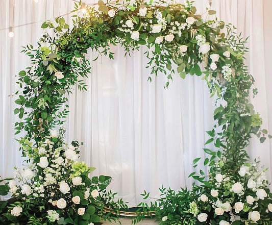 A circular floral arch adorned with white roses and greenery stands in front of white drapery, creating a Romantic Flower Wreath Bridal Wedding Backdrop-ideasbackdrop by ideasbackdrop that captures the scene in high-definition imagery.