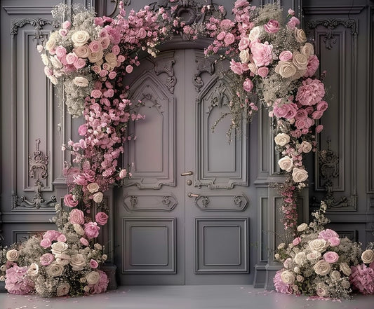 A gray double door is adorned with an elaborate floral arrangement featuring pink and white roses and greenery, extending from the floor to above the doorframe. The wall is ornately decorated, creating a scene of floral elegance with the Romantic Wedding Door Rose Flower Backdrop -ideasbackdrop by ideasbackdrop.