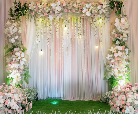 A decorated floral archway with pink and white flowers, greenery, and fabric drapes creates a stunning high-definition scene. Set on a green grassy surface with additional floral arrangements on both sides, this Romantic Wedding Floral Backdrop for Photography Studio by ideasbackdrop brings your event to life.
