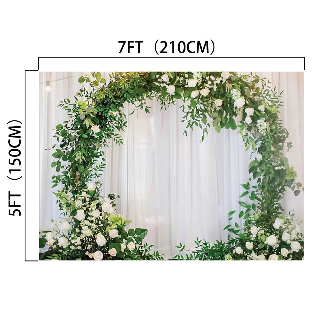 A circular floral arrangement featuring green leaves and white flowers, measuring 7 feet (210 cm) in width and 5 feet (150 cm) in height, set against a white curtain backdrop, creating a wedding backdrop for picture-perfect moments. Perfectly captured in HD vivid detail. The product is the Romantic Flower Wreath Bridal Wedding Backdrop-ideasbackdrop by ideasbackdrop.