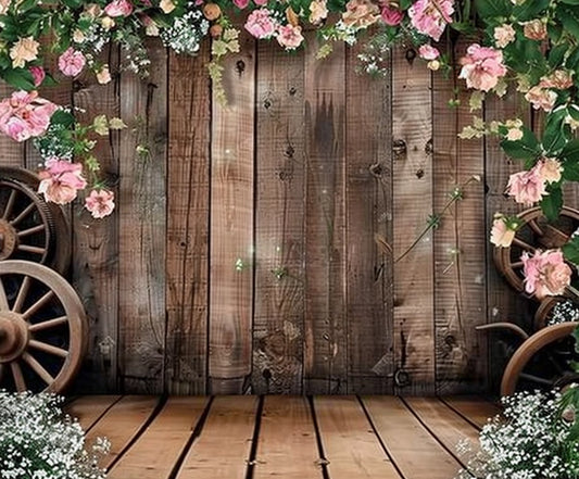 A Rustic Wood Barn Wall Leaves Flower Backdrop -ideasbackdrop decorated with pink flowers and greenery, accompanied by old wooden wagon wheels, creates a rustic setting perfect for photo opportunities.