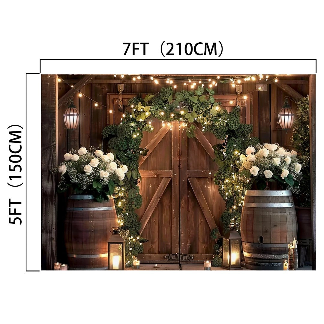 A rustic door decorated with greenery, vibrant hues of white flowers, and fairy lights, flanked by two large barrels. The Rustic Western Barn Door Floral Backdrop - ideasbackdrop measures 7FT (210CM) wide and 5FT (150CM) tall.
