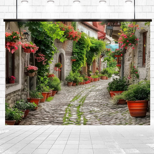 Cobblestone street lined with flowers and plants in pots, creating a Spring Alleyway Potted Flowers Backdrop -ideasbackdrop as it winds between rustic, ivy-covered buildings by ideasbackdrop.