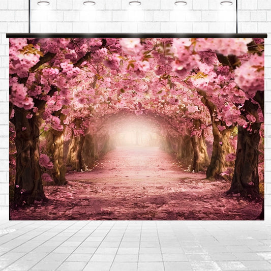 A backdrop of an archway formed by blooming cherry blossom trees, creating a tunnel effect with a light at the distant end. The scene has a soft, pink hue throughout, making it perfect for professional photography or as an elegant event backdrop. This is the Spring Cherry Blossom Tree Boulevard Floral Backdrop by ideasbackdrop.