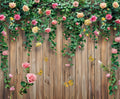 A wooden fence decorated with climbing rose vines bearing HD flowers in pink and yellow, with several butterflies fluttering around, serves as a perfect Spring Floral Wood Plank Photoshoot Flowers Backdrop -ideasbackdrop for event decorators by ideasbackdrop.
