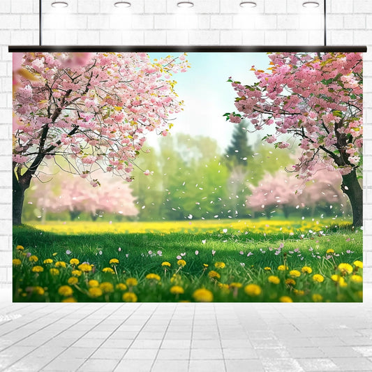 Colorful spring scene with cherry blossom trees in full bloom and yellow flowers on a grassy field. White petals are falling from the trees, adding a delicate floral touch. The background features a lush, green, out-of-focus forest, creating sophisticated photo opportunities with the Spring Landscape Meadow Flower Backdrop by ideasbackdrop.