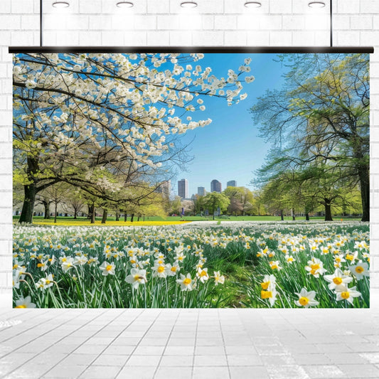 A bright spring day in a park with green grass, blooming white flowers creating a Spring Scenery Garden Blossom Flowers Backdrop-ideasbackdrop, and trees, with a city skyline visible in the background under a blue sky.