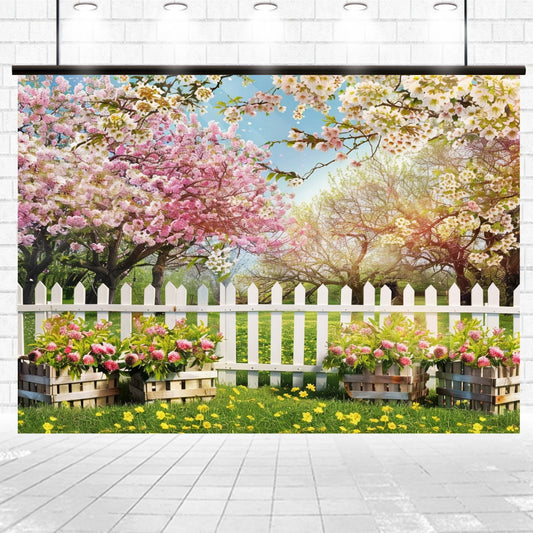 A serene retreat with a white picket fence surrounded by lush green grass and blooming cherry blossom trees. Flower boxes with pink and white flowers are placed along the fence, creating a beautiful floral backdrop, including the Spring White Forest Tree Flower Backdrop from ideasbackdrop. The sky is clear and blue.
