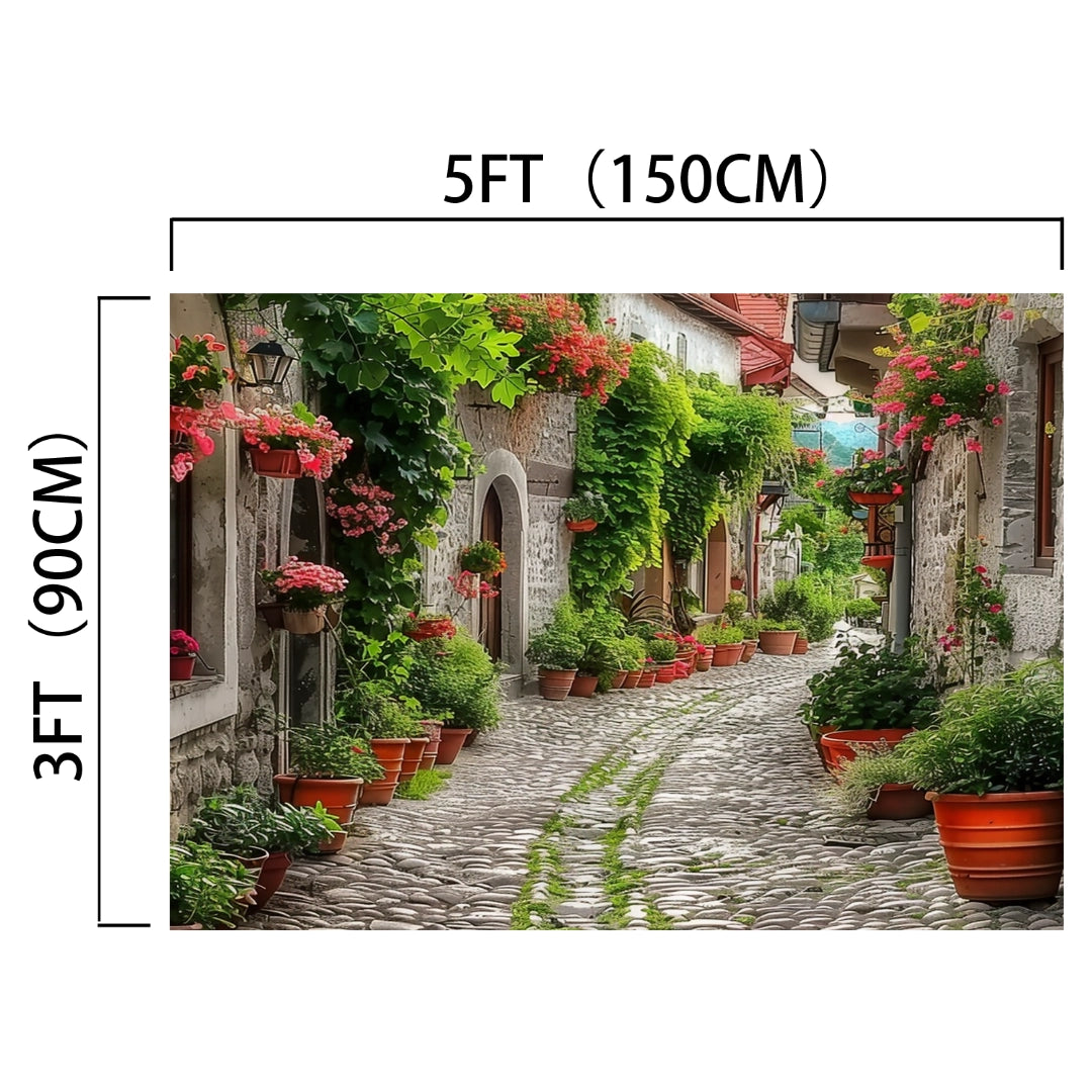 Cobblestone alley lined with potted plants and flowers, creating a floral paradise. Overhanging greenery adorns buildings, adding lifelike detail. Dimensions are 5 feet (150 cm) wide and 3 feet (90 cm) tall, making it an Spring Alleyway Potted Flowers Backdrop -ideasbackdrop perfect for stunning visuals.