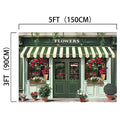 Image of a storefront with a green and white striped awning, labeled "FLOWERS," measuring 5 feet (150 cm) wide and 3 feet (90 cm) tall. The storefront, captured in high-resolution imagery, is decorated with various potted plants and flowers, bathed in natural light that highlights the vibrant colors. This scene features the Spring Flower Market Bloom Window Backdrop-ideasbackdrop by ideasbackdrop.