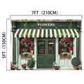 Exterior view of a flower shop with a green and white striped awning. The shop, bathed in natural light, is adorned with various potted flowers. Dimensions indicated are 7 feet (210 cm) wide and 5 feet (150 cm) tall, perfect for a Spring Flower Market Bloom Window Backdrop-ideasbackdrop by ideasbackdrop or high-resolution imagery.