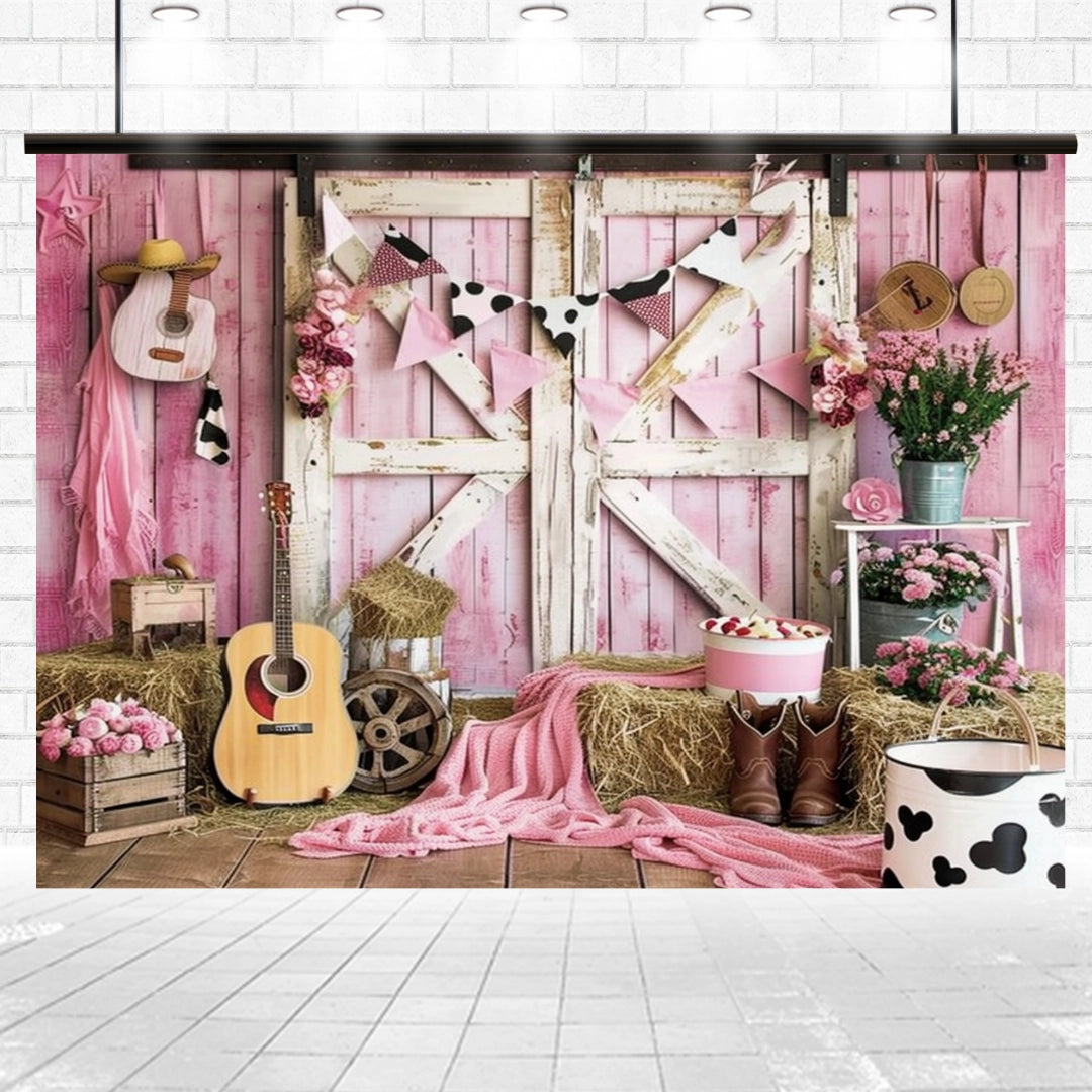 A rustic setup radiates countryside vibes with two guitars, hay bales, a Western Cowgirl Wild West Rustic Barn Backdrop-ideasbackdrop by ideasbackdrop, a wooden wagon wheel, cow-patterned decorations, pink flowers, boots, and various pink accessories arranged around a charming barn door.