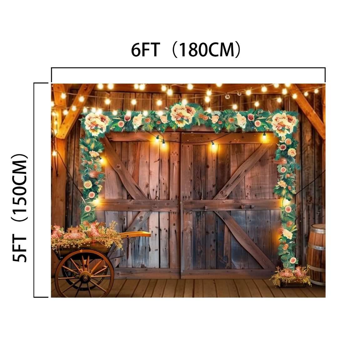 Wooden double doors adorned with floral garland, string lights, and hanging lights exude rustic elegance. Dimensions: 6 feet (180 cm) wide, 5 feet (150 cm) tall. In front, a wooden cart with flowers completes the countryside barn aesthetic akin to an ideasbackdrop Western Cowboy Floral Wood Barn Barn Backdrop-ideasbackdrop.