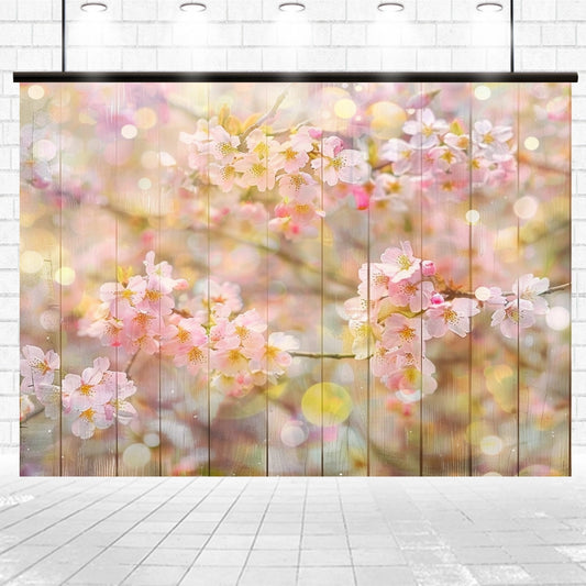 A wall mural features a serene scene of photorealistic florals with pink cherry blossoms in bloom and soft bokeh lighting effects, framed within a white brick space and illuminated from above, showcasing the Wood Wall Spring Blossom Pink Flower Backdrop-ideasbackdrop by ideasbackdrop.